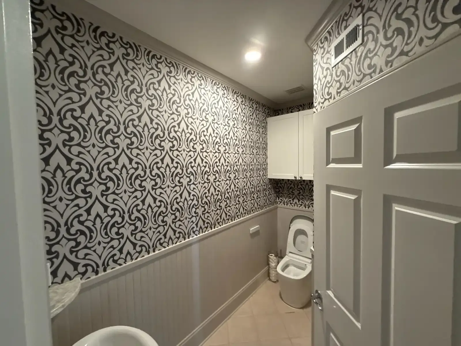 Black and white damask wallpaper above beadboard in a bathroom