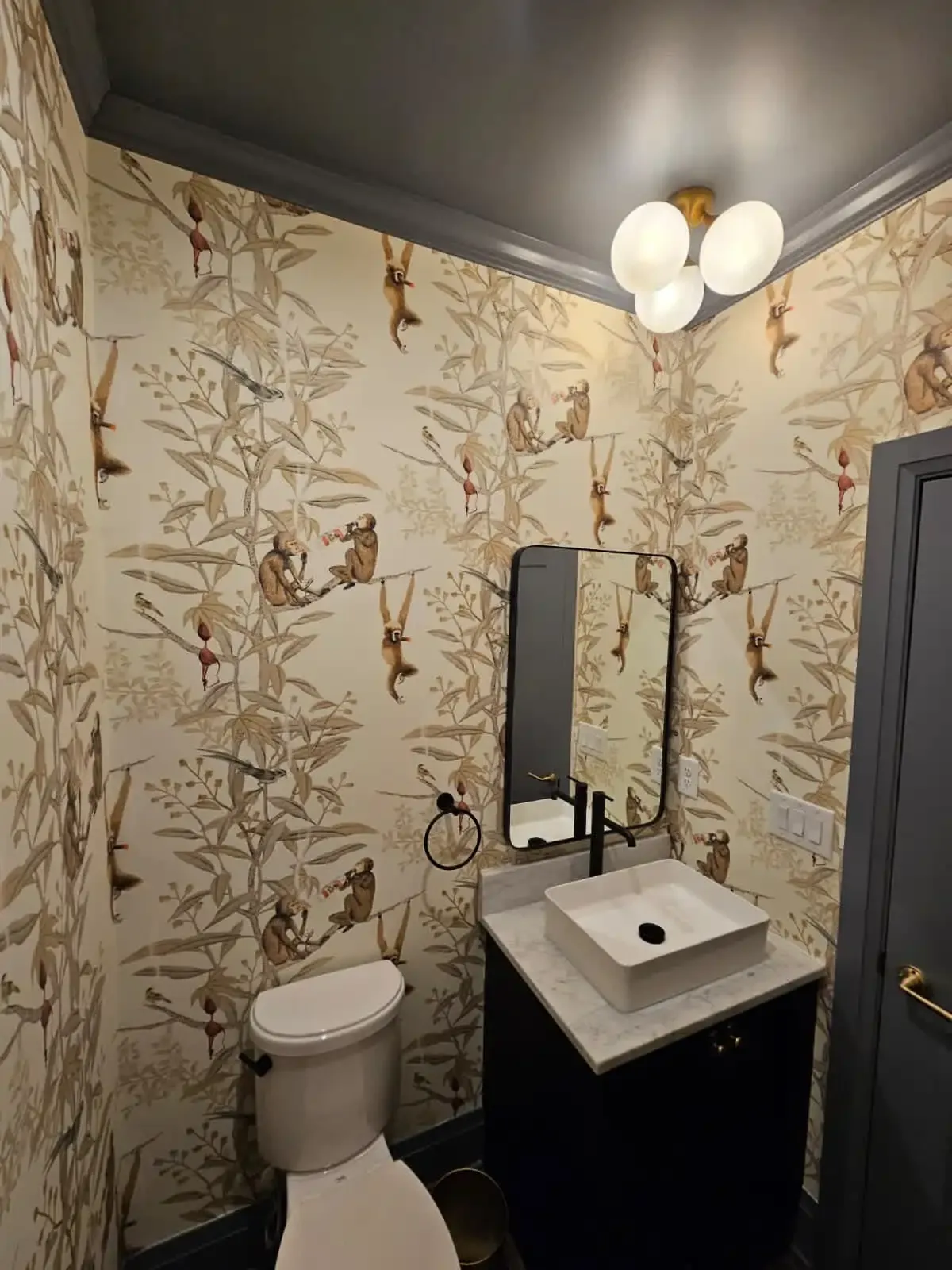 Monkey toile wallpaper in a powder room with a dark vanity and black mirror